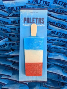 Paleta Factory’s red, white, and blue paleta, featuring strawberry, lime, and blue raspberry flavors, in individually wrapped signature blue packaging.