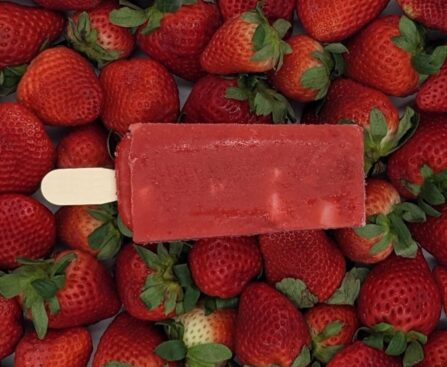 Strawberry paleta made with real fruit resting on a bed of fresh strawberries